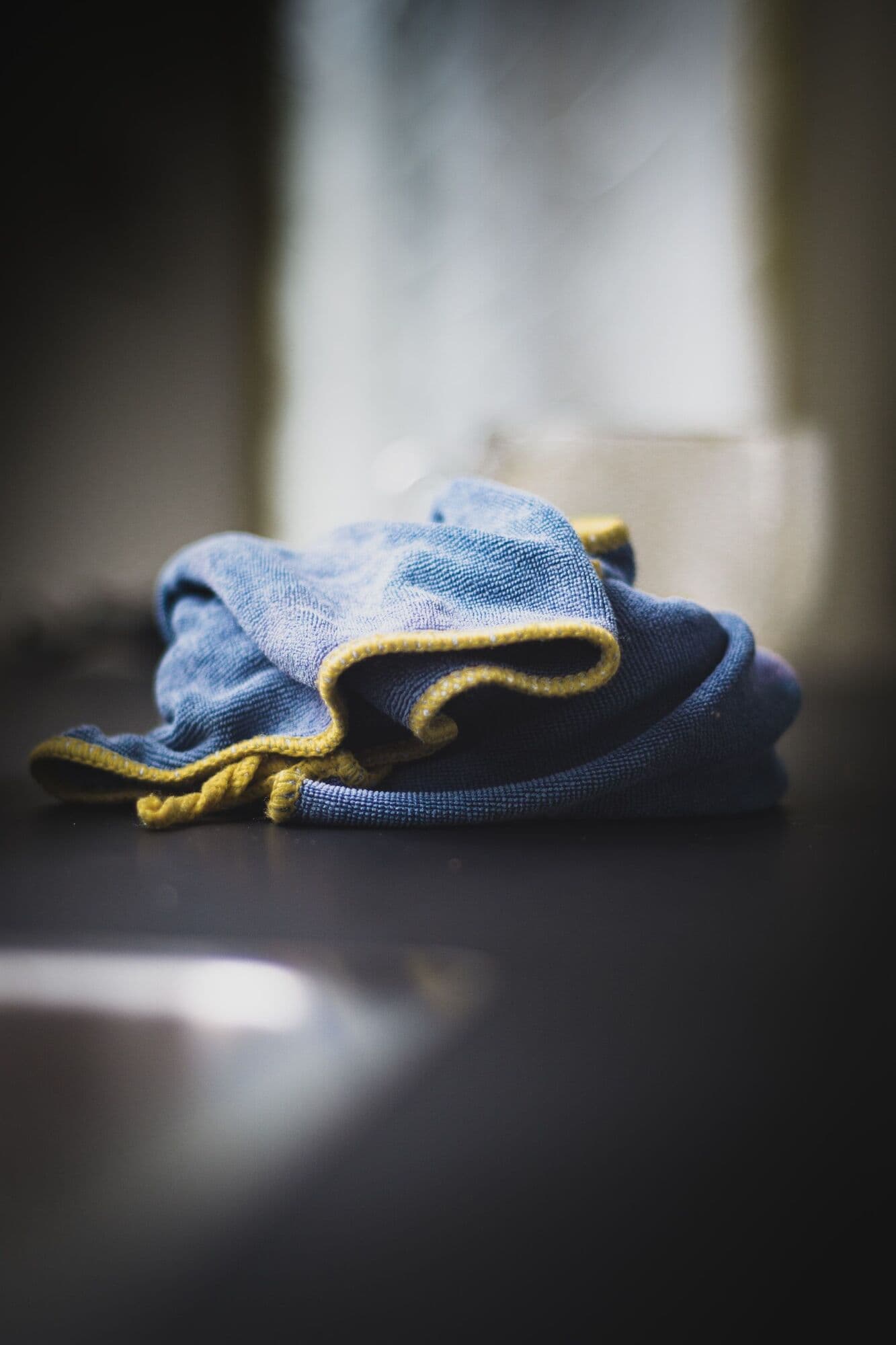 Blue microfibre cloth with a yellow edge on a dark surface.